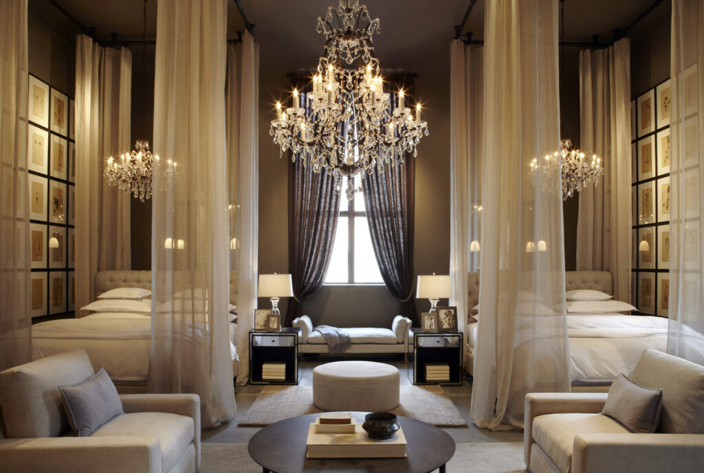 Restoration Hardware bedroom display with draped canopy beds, crystal chandeliers, neutral tones, and classic interior design details.