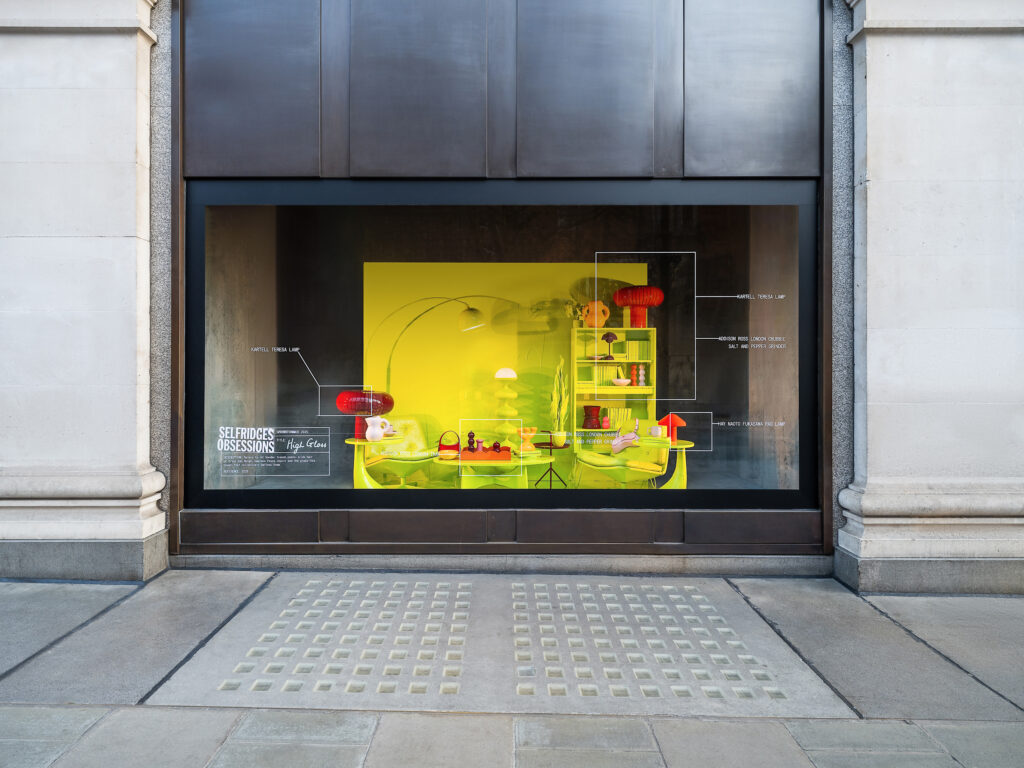 Bright yellow Selfridges Obsessions window display titled High Gloss, showcasing modern homeware, lighting, and fashion accessories.