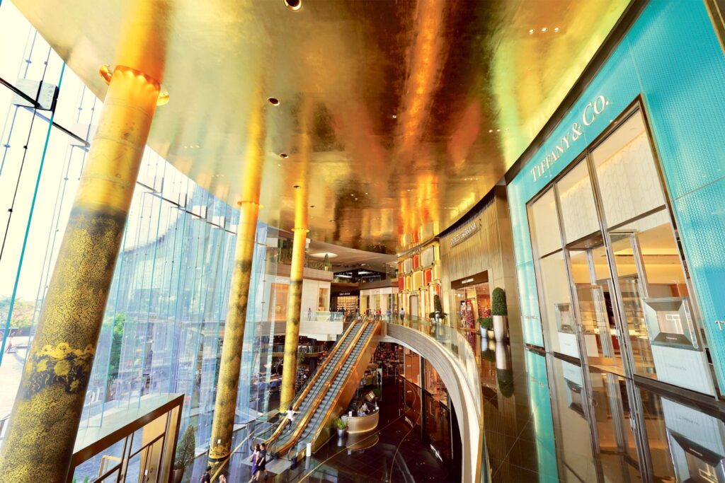 ICONLUXE Zone at ICONSIAM, displaying a grand, gold-toned interior with reflective ceilings, patterned columns, and high-end boutiques such as Tiffany & Co. and Dolce & Gabbana.