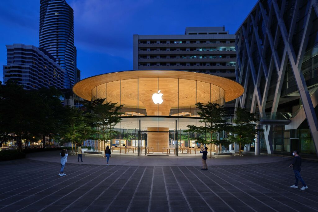Apple Central World store in Bangkok, showcasing a circular glass structure with a wooden roof, illuminated at night amid surrounding skyscrapers.
