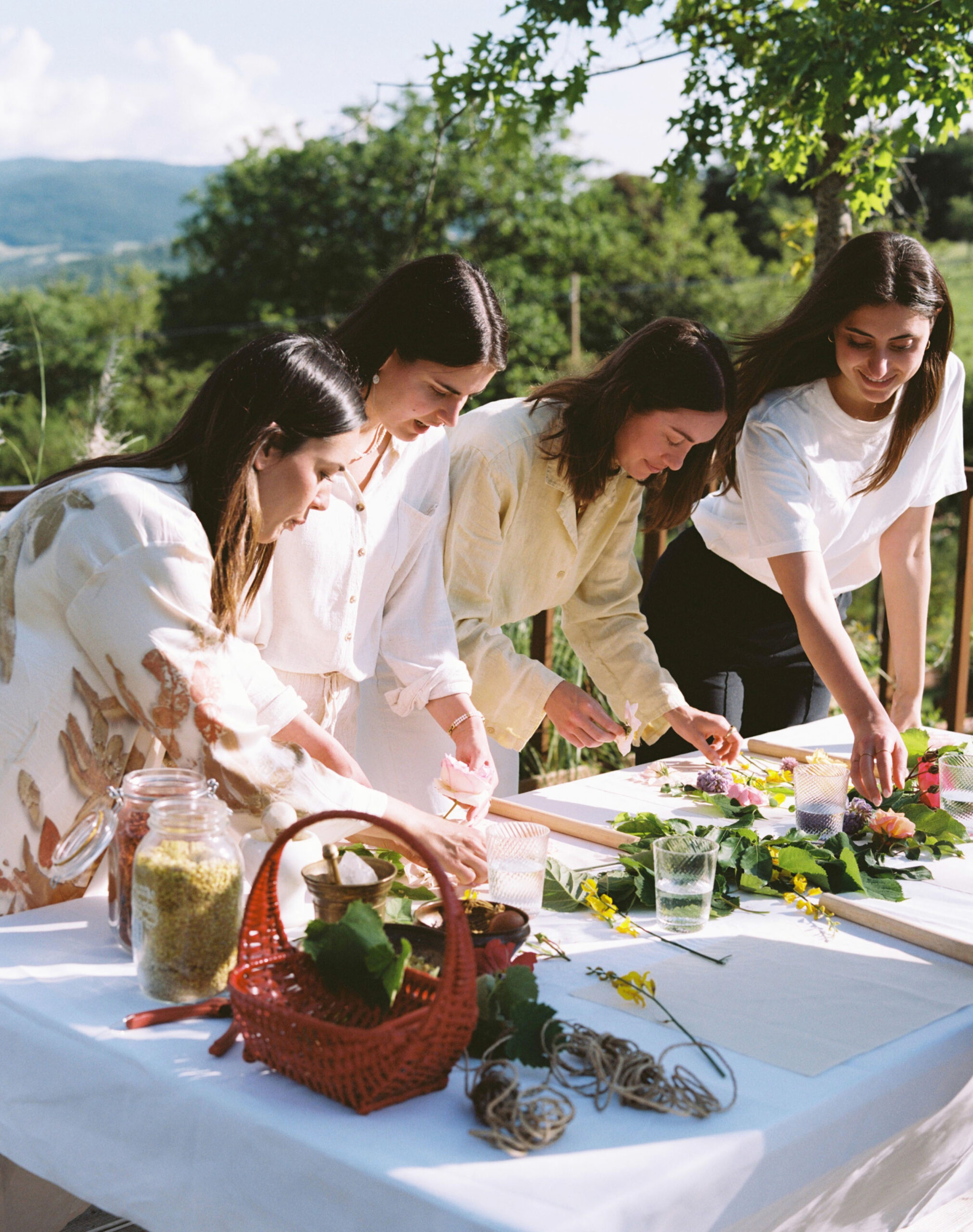Group of women participating in an eco-printing and botanical art workshop at Castello di Casole in Tuscany, arranging flowers and natural materials outdoors under sunlight with scenic countryside views.
