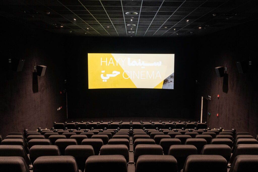 Interior of Hayy Cinema in Jeddah, a modern screening hall with minimalist black interiors and the Hayy Cinema logo illuminated on screen.