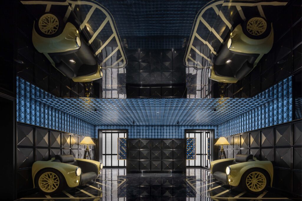 Luxurious restroom interior with a bold automotive-inspired design, featuring car-shaped chairs, geometric wall panels, and reflective blue ceilings.