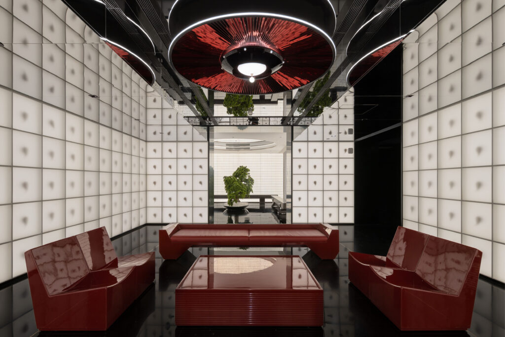Minimalist restroom design with red lacquer furniture, illuminated white wall panels, and a central bonsai tree creating a calm, modern ambience.
