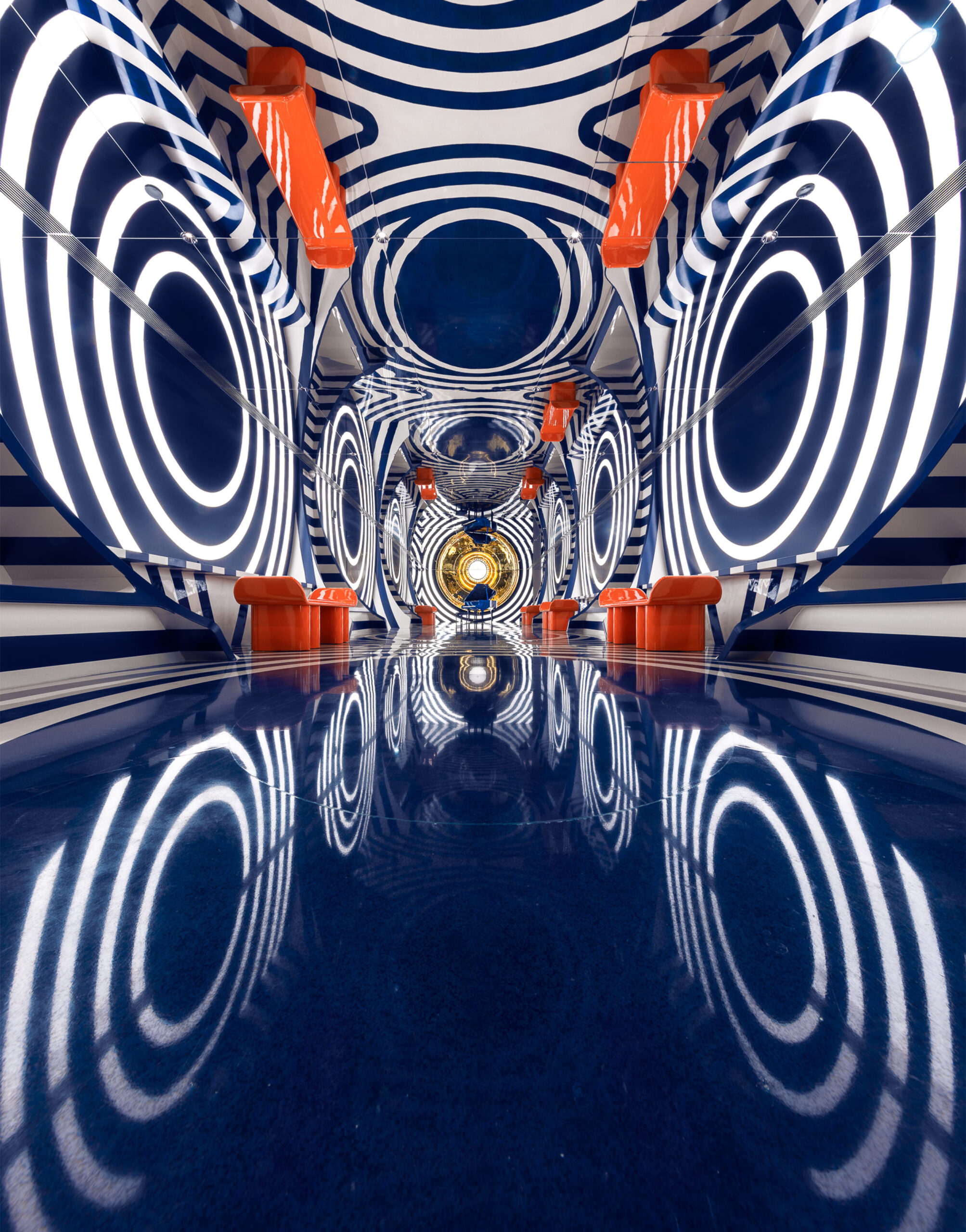 Vibrant interior with bold concentric patterns in blue and white, red seating, and reflective finishes inspired by pop art and optical illusion design.