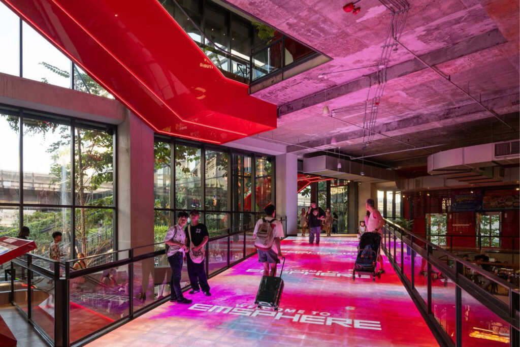Entrance interior of Emsphere Bangkok with illuminated pink and red floors, modern industrial ceiling design, and visitors walking through the welcoming retail space.