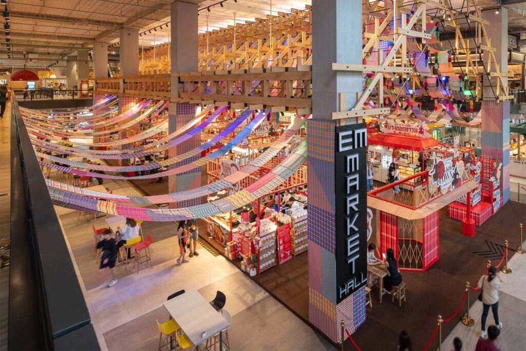 Interior of Emsphere Bangkok’s market hall with colourful textile installations, wooden structures, and food stalls creating a lively and creative retail environment.