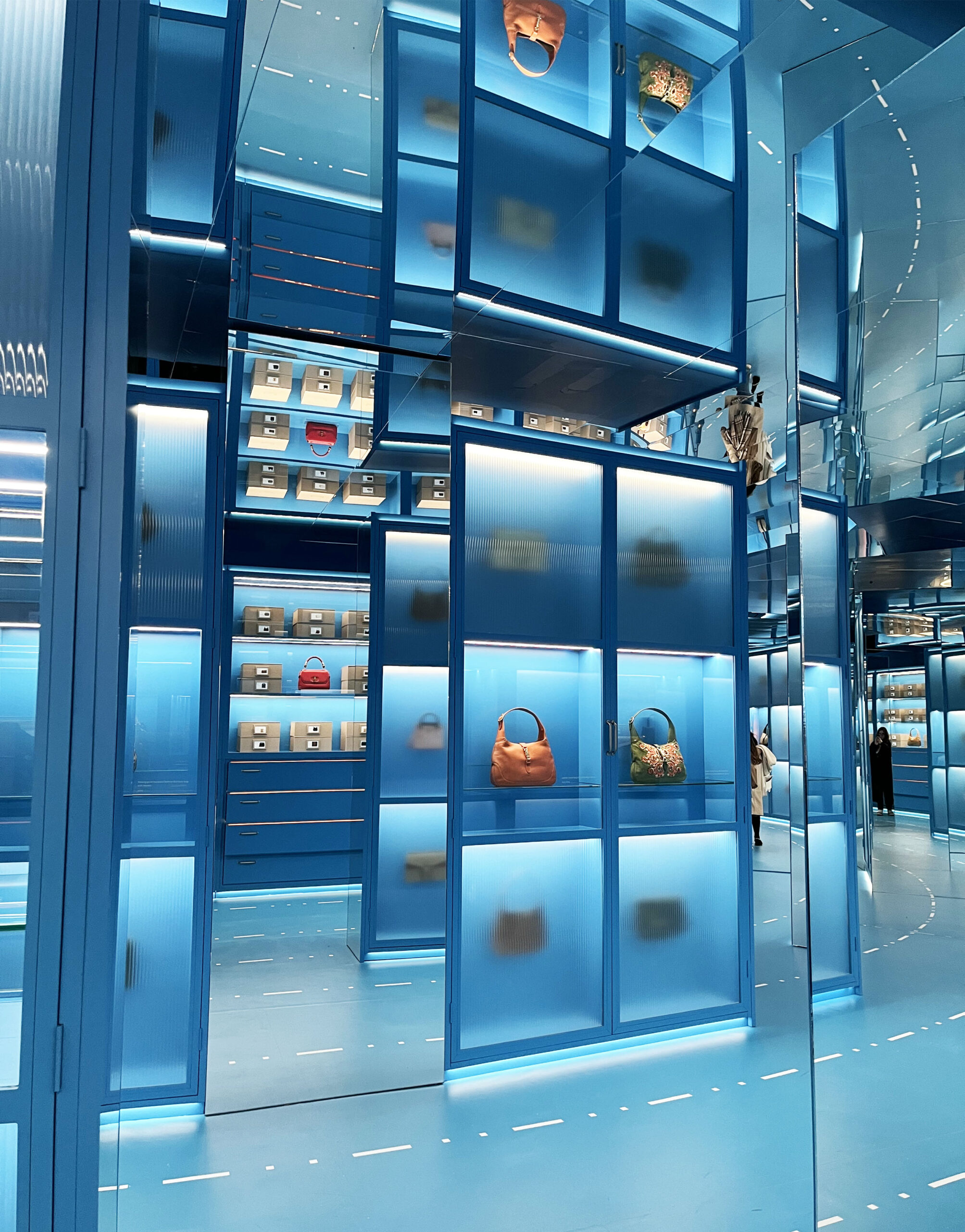 Gucci Cosmos exhibition space featuring illuminated blue display cases showcasing handbags and archival pieces in a futuristic, mirrored environment.