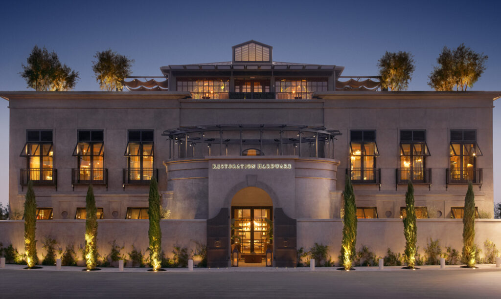 Evening view of Restoration Hardware storefront with warm lighting, symmetrical façade, and contemporary architectural design.