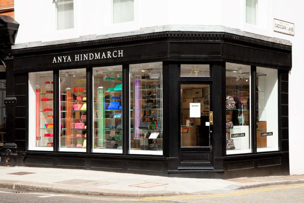 Exterior of the Anya Hindmarch Labelled store on Cadogan Lane, London, featuring a black-painted shopfront with colorful handbags displayed in illuminated glass shelves.