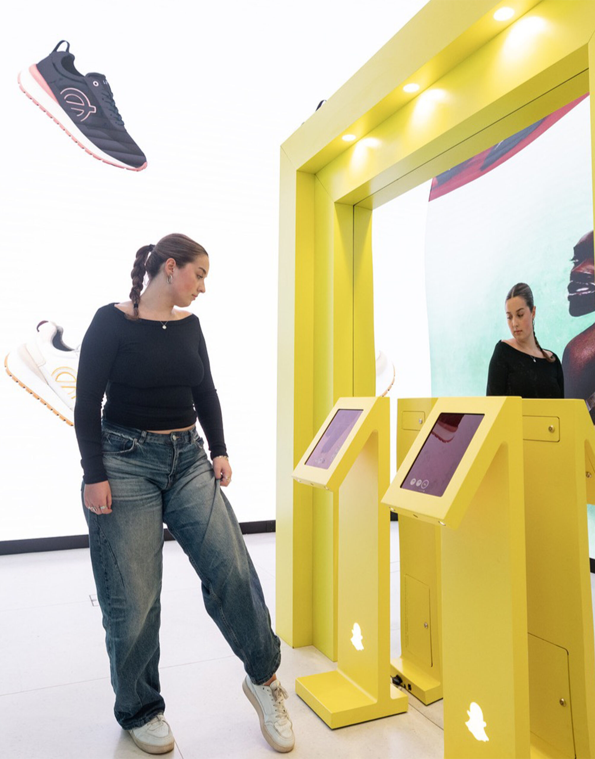 Customer using a virtual try-on experience through augmented reality technology at a bright yellow digital kiosk in a futuristic sneaker retail store.