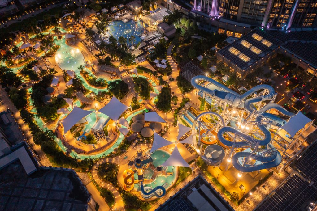 Aerial night view of the Galaxy Macau Grand Resort Deck, showcasing its illuminated water park with interconnected pools, water slides, and tropical landscaping creating a vibrant resort atmosphere.
