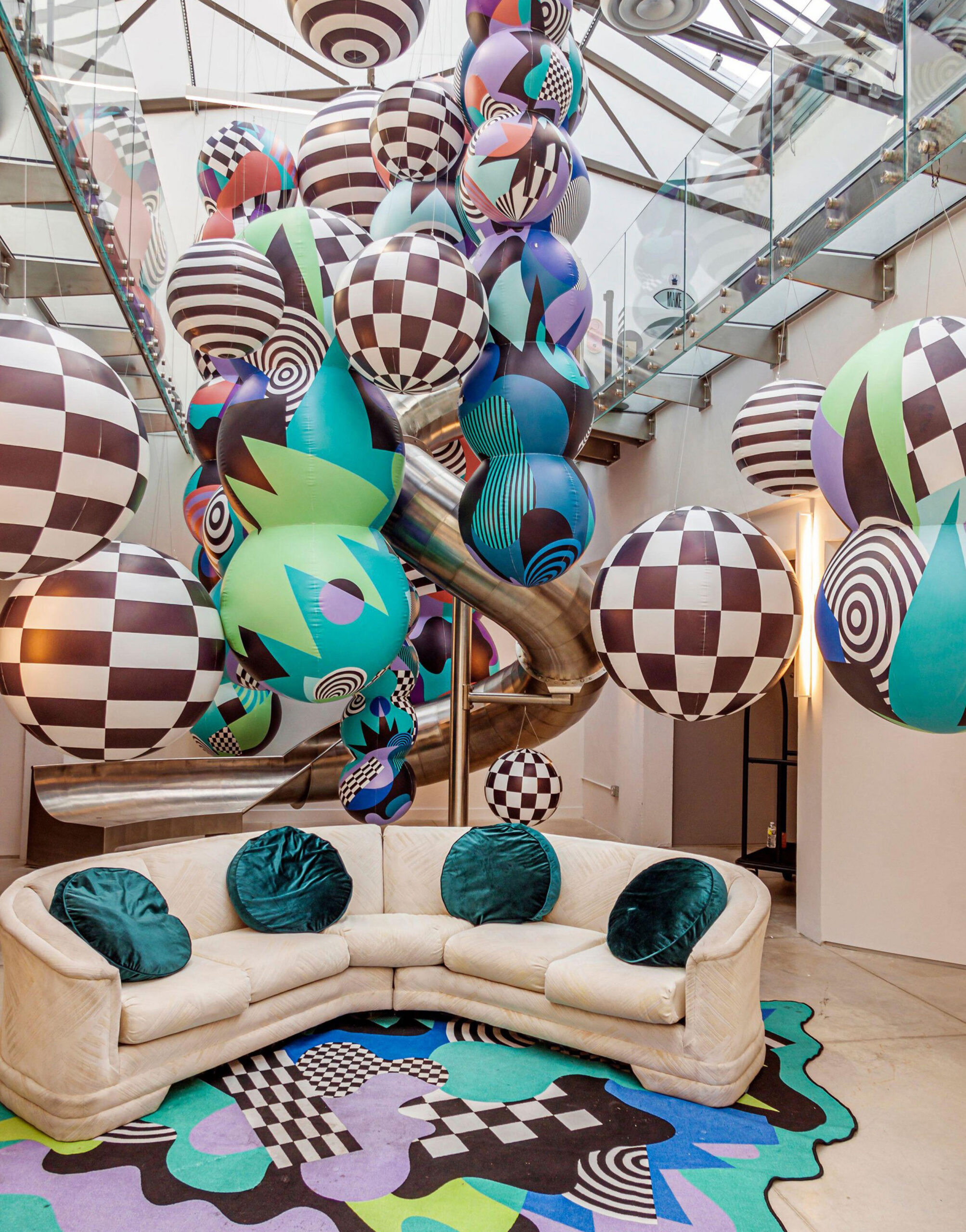 Interior of Showfields department store featuring colorful geometric balloons, modern art-inspired decor, and a curved sofa beneath a glass ceiling.