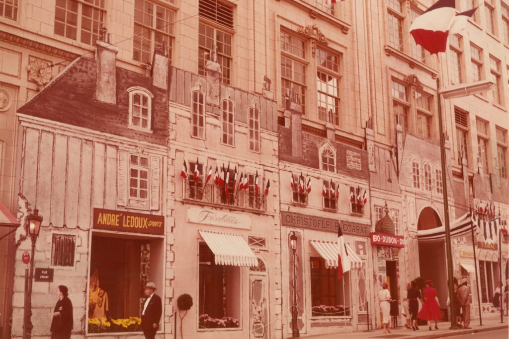 Historic Neiman Marcus façade decorated for French Fortnight, featuring Parisian-style storefront designs, French flags, and shoppers along the street.