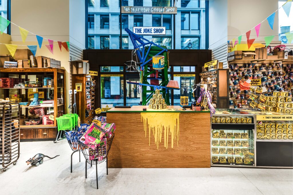 Inside The Joke Shop at Selfridges Corner Shop, featuring colourful props, retro packaging, and vibrant installations.