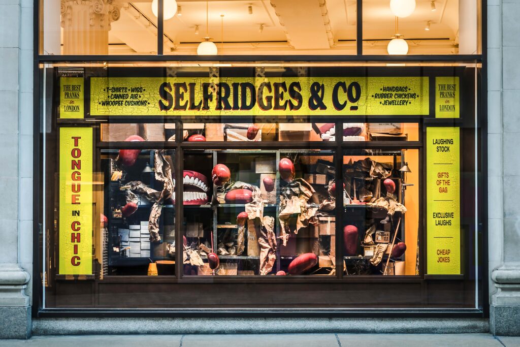Selfridges window display for The Joke Shop with bold yellow signage, playful visuals, and humorous themed décor.