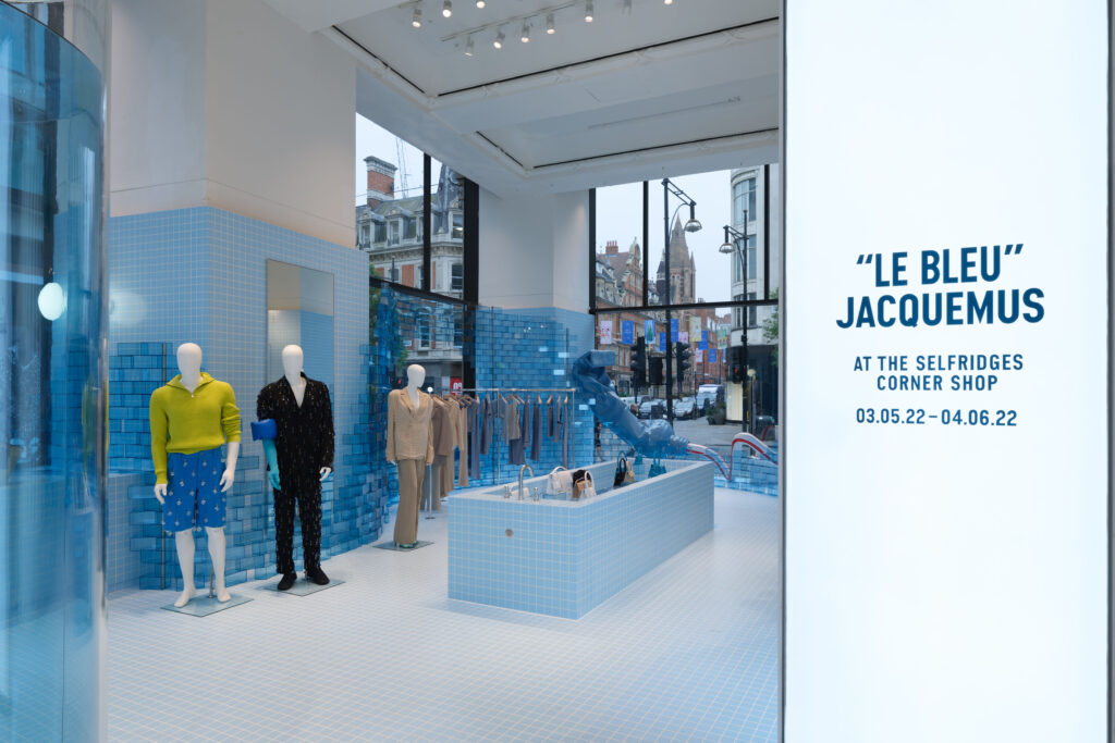 Interior of Jacquemus’ “Le Bleu” pop-up at Selfridges designed to resemble a modern swimming pool, with blue tiled floors, cylindrical water tank, mannequins, and floating handbag displays.
