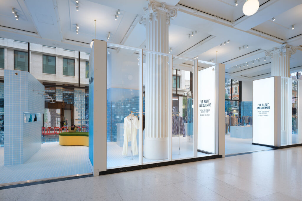 Indoor-facing view of the Jacquemus “Le Bleu” store at Selfridges, showing mannequins dressed in pastel tones and a tiled pool-inspired display under signage with the exhibition dates.