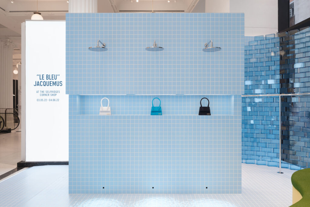 Detail view of the Jacquemus “Le Bleu” installation at Selfridges, where blue-tiled walls and white columns frame minimalist fashion displays in a bright, modern gallery setting.