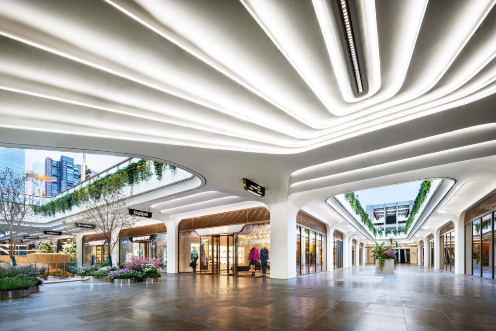 Interior courtyard of SKP Chengdu with fluid, organic ceiling lighting and greenery cascading from the upper level, creating a natural connection between indoor and outdoor spaces.