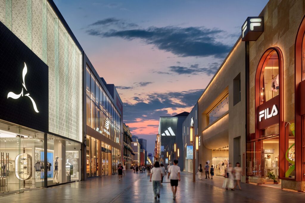 Street-level view of K-Avenue at SKP Wuhan, a contemporary retail promenade lined with fashion brands such as Fila and Adidas, bathed in the warm light of sunset.