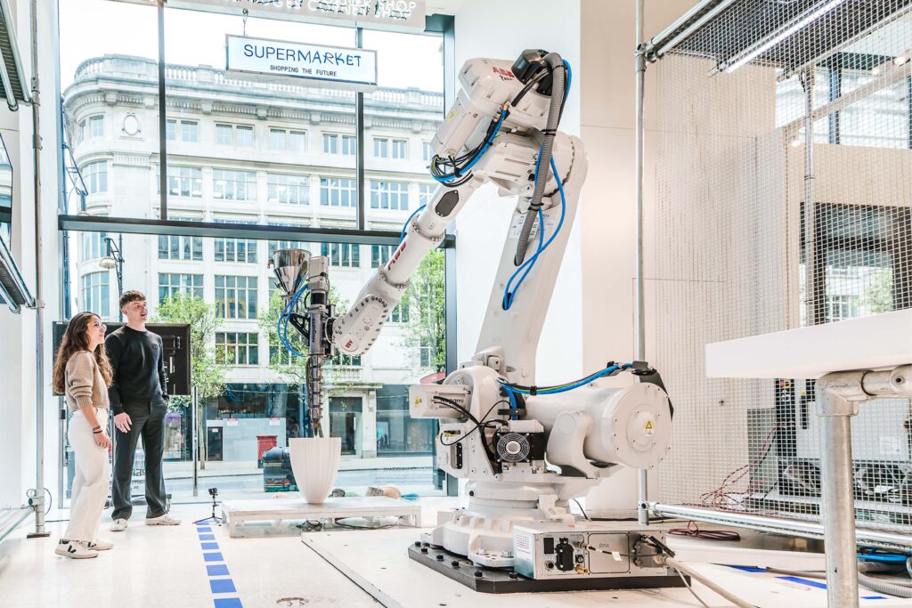 Visitors observe a robotic installation inside Selfridges’ Supermarket at The Corner Shop, showcasing future-focused retail innovation.