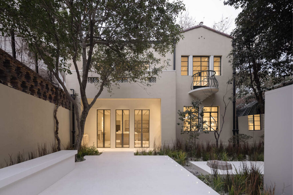 Exterior of To Summer Shanghai boutique at dusk, showing a cream-toned villa with large windows, a small balcony, and a landscaped courtyard with soft lighting.