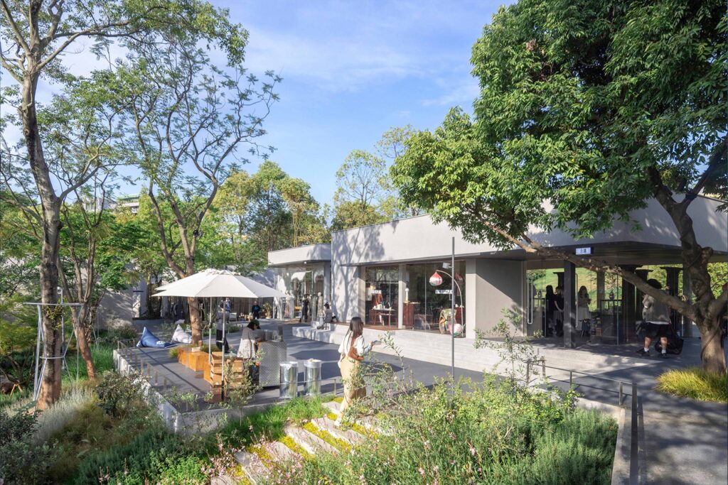 Open-air lifestyle space with minimalist concrete structures, outdoor seating, and people enjoying a landscaped garden environment.