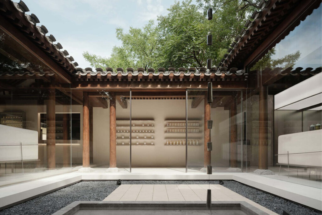 Courtyard of To Summer Beijing enclosed by glass and wooden beams, centered around a minimalist gravel garden that connects the interior spaces.