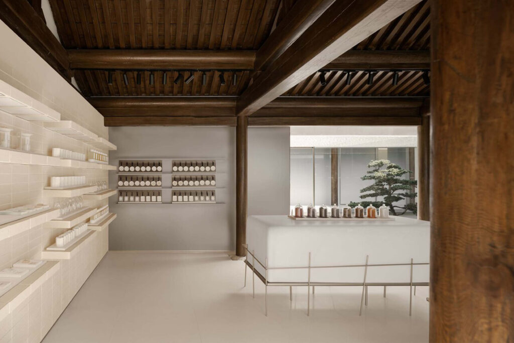 Interior of To Summer Beijing featuring wooden beams, minimalist shelving with neatly arranged products, and a serene bonsai tree visible through the window.